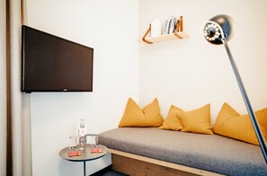 A modern room with a bed, a mounted TV, a small table with a glass, a bottle, and a lamp. - Basic double rooms (16m²) - Hotel & Restaurant Alpenrose Bayrischzell (Bayrischzell)