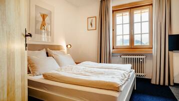 Ein Hotelzimmer mit Bett, einem Vorhangfenster, einem Heizkörper und einem gerahmten Bild an der Wand.
