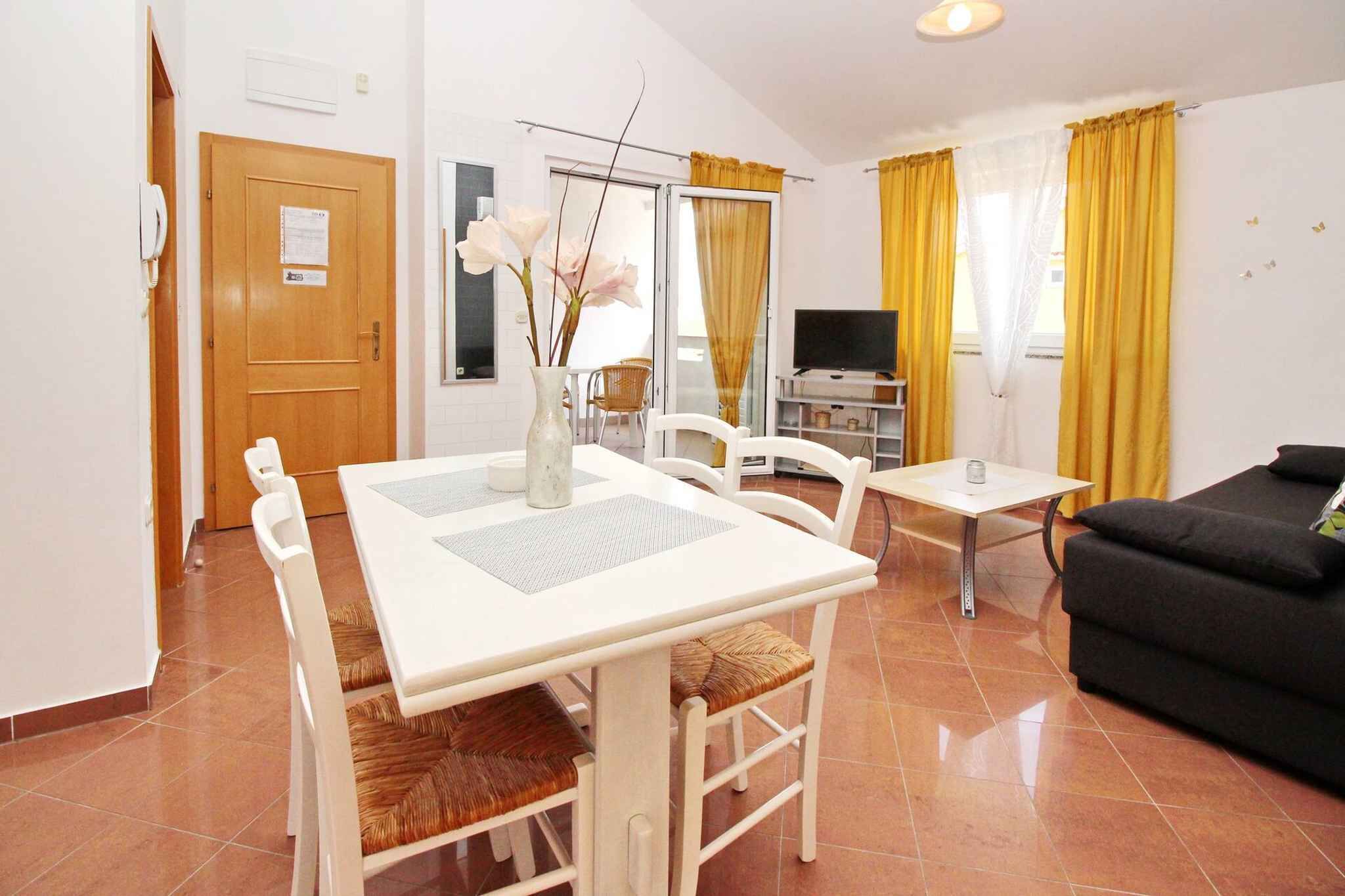 A dining area with a white table and chairs, a vase with flowers, a TV, and yellow curtains.
