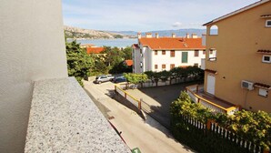 Zona residenziale con vista su strada, che include un edificio con tetto in tegole rosse, auto parcheggiate e una chiara vista del mare sullo sfondo.