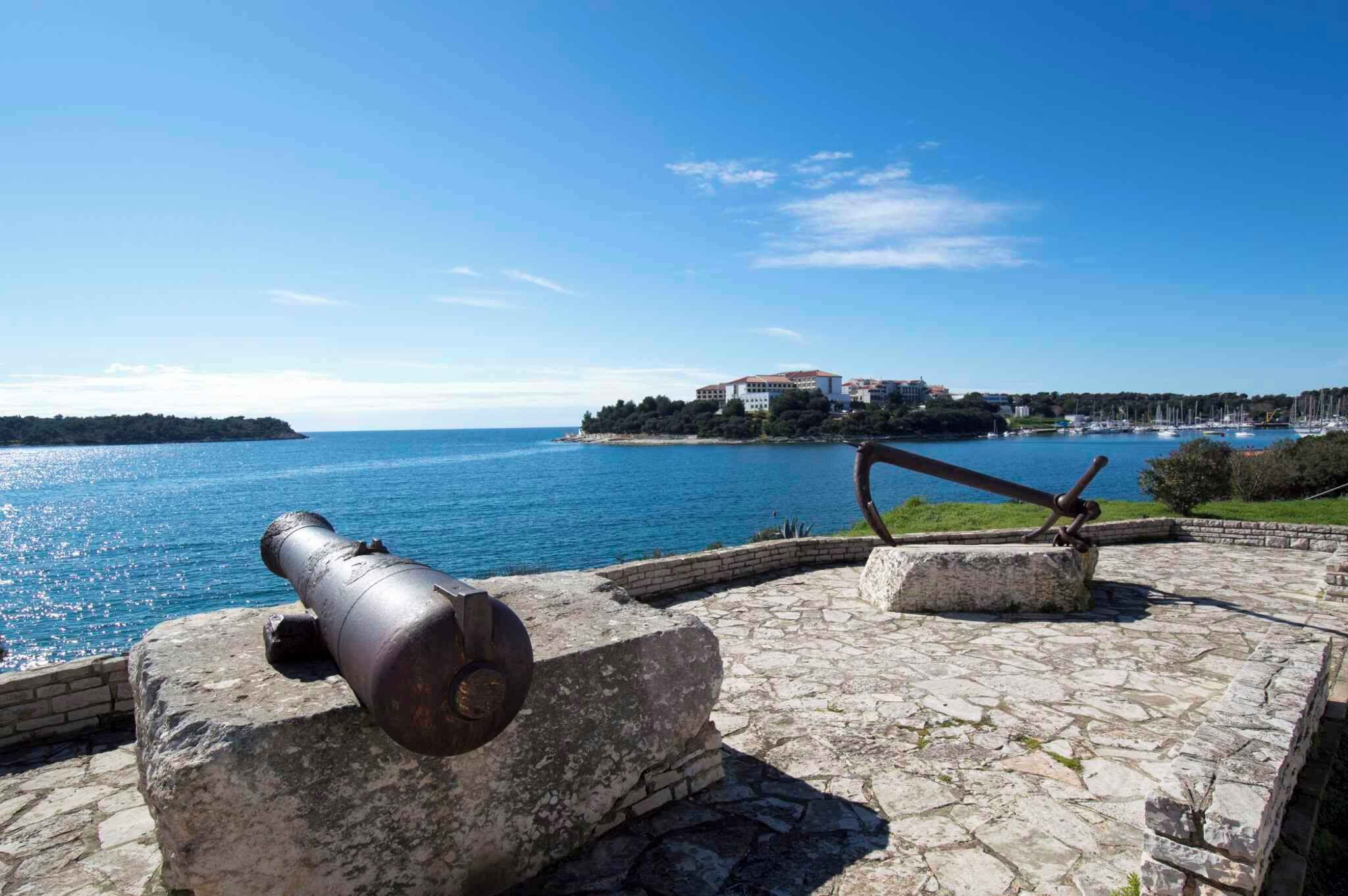A stone pathway leading to a historic cannon overlooking a coastal town with a clear blue sky.