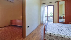 A hotel room with a wooden floor, a bed with a patterned bedspread, a wardrobe, and a sliding glass door leading to a balcony with outdoor furniture. - Holiday apartment with balcony (Pješćana Uvala)