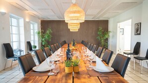 Konferenssihuone, jossa on pitkä puinen pöytä, mustat tuolit ja katosta roikkuva valaisin.