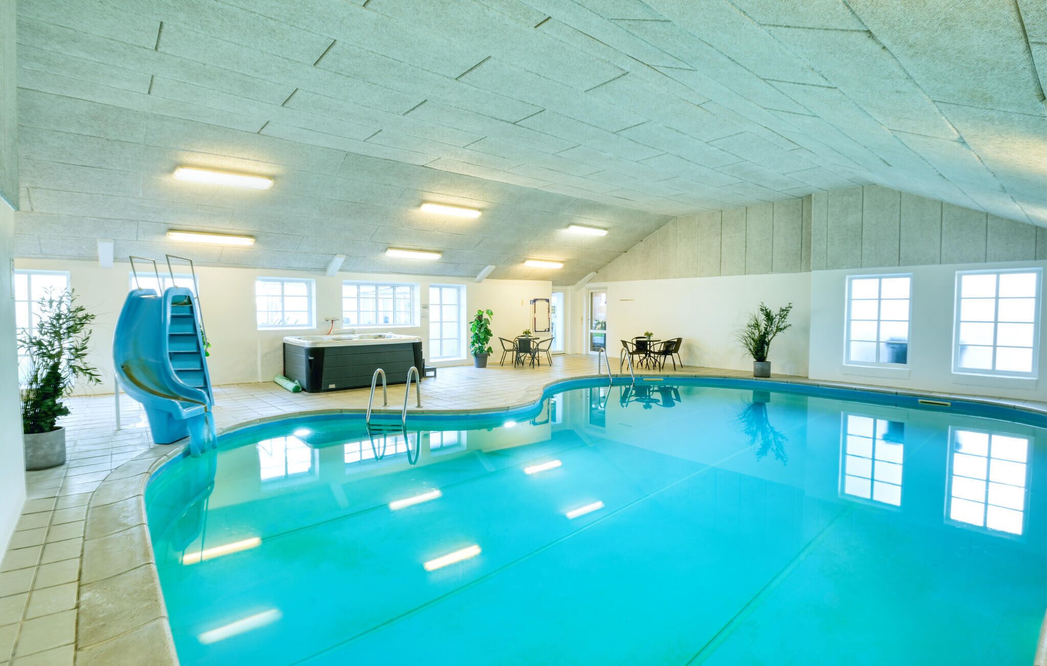 An indoor swimming pool with a slide, hot tub, and seating area.