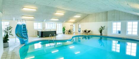 An indoor swimming pool with a slide, hot tub, and seating area.
