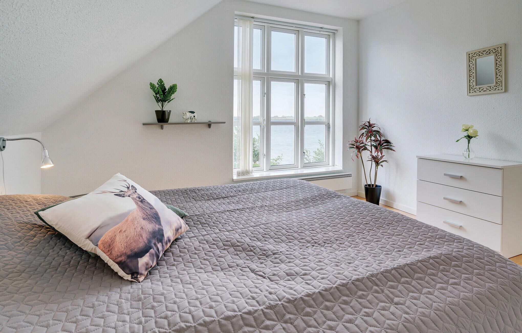 A bedroom with a large bed, a window with a view, a bedside table, and a dresser.