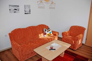 Una habitación con un sofá naranja y un sillón a juego, una pequeña mesa de madera y dos lámparas fijadas a la pared.