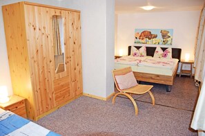 Un dormitorio con un armario de madera, una cama con ropa de cama floral, una silla y un cuadro en la pared.