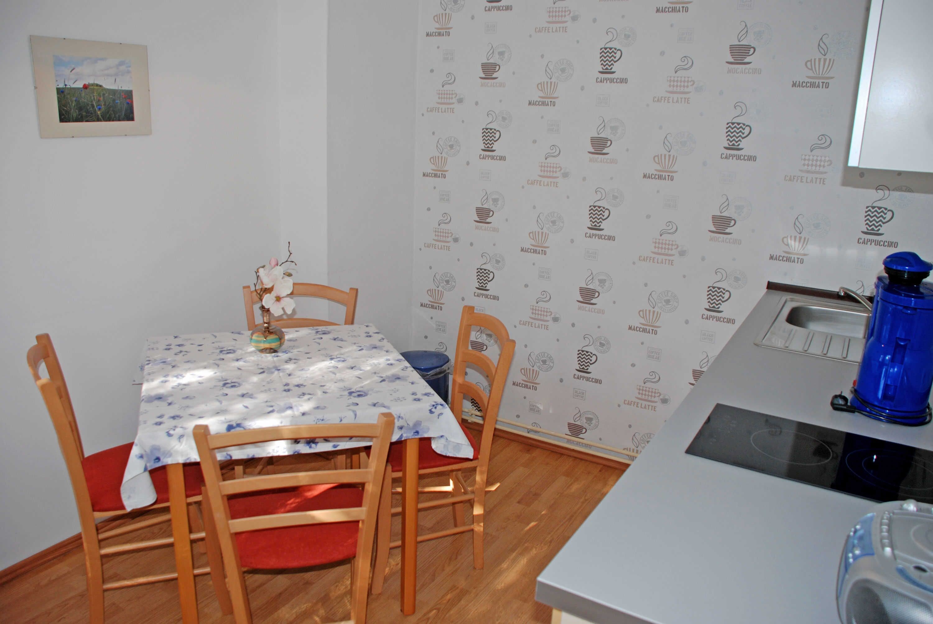 A small dining area with a table covered by a floral tablecloth, wooden chairs, and a blue water dispenser on a counter.