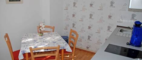 A small dining area with a table covered by a floral tablecloth, wooden chairs, and a blue water dispenser on a counter.