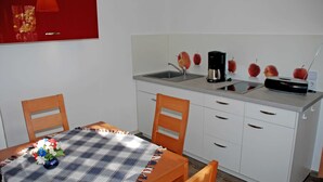 A small kitchenette with a sink, a coffee maker, and a radio. There is a table with a checkered tablecloth and a vase of flowers. - Apartment OG - Apartments on the Heideweg (Baabe)