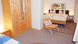 A bedroom with a wooden wardrobe, a bed with floral bedding, a chair, and a painting on the wall. - Apartment OG - Apartments on the Heideweg (Baabe)