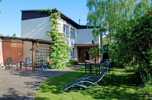 A building with a white exterior, a wooden door, and a small garden area with chairs and a table.