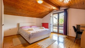 A bedroom with a wooden ceiling, a bed with a floral bedspread, two rugs, a red radiator, and a view of the outside through a glass door.