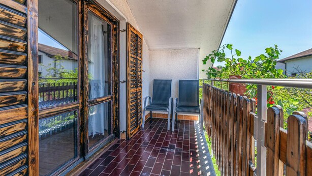 A balcony with a wooden fence, two striped chairs, and a potted plant.