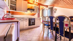 A modern kitchen with white cabinets, a built-in oven, and a dining area with blue chairs and a colorful tablecloth.