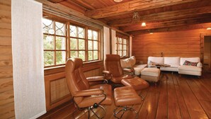 A log cabin interior with leather chairs, a white sofa, and large windows.