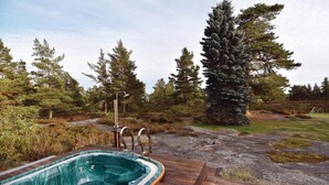 A hot tub on a wooden deck with a showerhead, surrounded by a natural landscape with trees and a path.