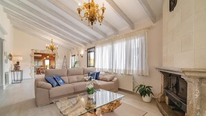 A spacious living room with a beige sofa, a glass coffee table with a wooden base, a fireplace, and a chandelier. - Lovely home in Muro with private swimming pool, can be inside or outside (Muro)