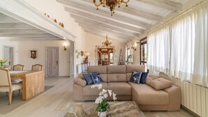 A spacious living room with a large beige sectional sofa, a wooden coffee table, and a chandelier. - Lovely home in Muro with private swimming pool, can be inside or outside (Muro)