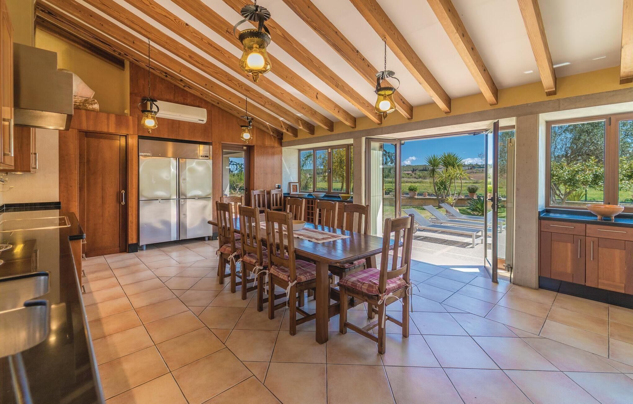 A spacious kitchen with wooden cabinets, a dining area with a large table and chairs, and a view of the outdoors through large sliding glass doors. - Lovely home in Muro with private swimming pool, can be inside or outside (Muro)