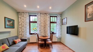 A living room with a sofa, a dining table with chairs, a TV mounted on the wall, and a window with curtains. - Labedz (LA16) - LA16 (Swinoujscie)