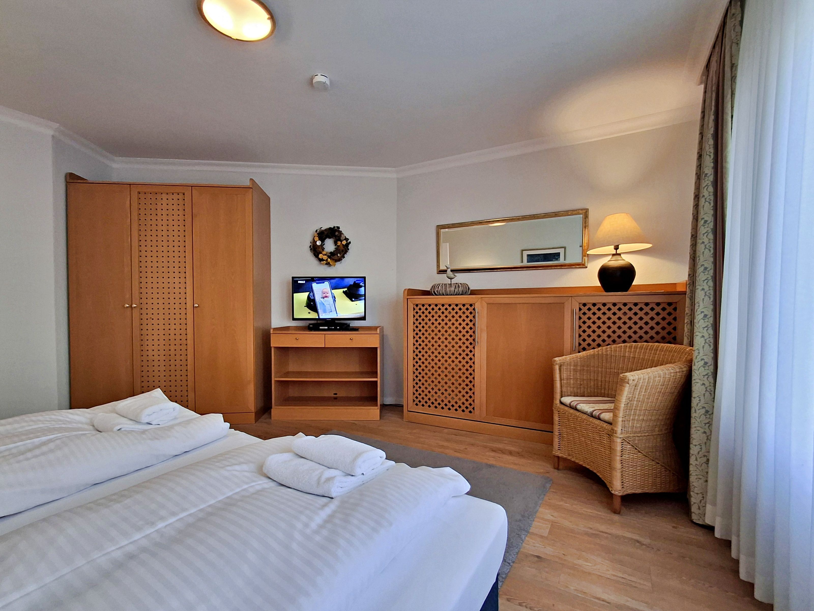 A hotel room with two beds, a desk with a computer, a chair, a wardrobe, and a mirror.