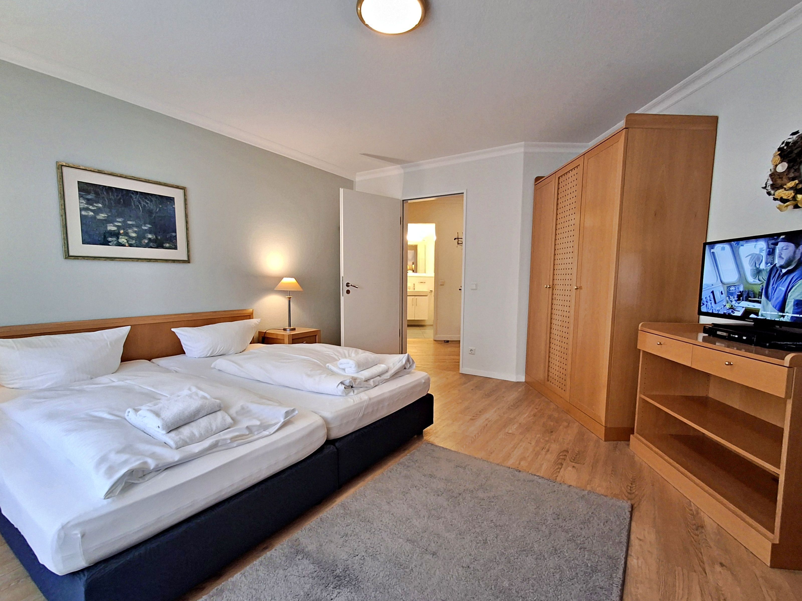 Une chambre d’hôtel avec un lit double, une télévision, une armoire en bois et un tableau encadré au mur.