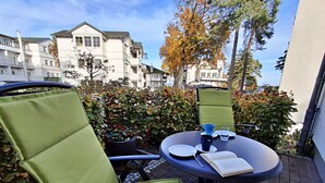 Une terrasse avec deux chaises vertes, une table et un livre.