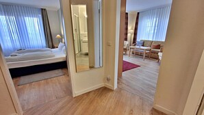 Une chambre d’hôtel avec un lit, un miroir, un plancher en bois, un canapé et une petite table.
