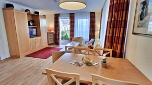 Une chambre d’hôtel moderne avec une table à manger en bois, des chaises, un téléviseur, une lampe et une vue sur l’extérieur grâce à de grandes fenêtres.