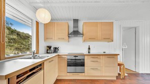 A modern kitchen with wooden cabinets, a built-in dishwasher, and a large window overlooking a natural landscape. - Lovely home in Hvide Sande with WiFi (Hvide Sande)
