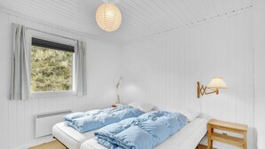 A bedroom with two beds, a window with curtains, a radiator, a bedside lamp, and a wall-mounted lamp. - Lovely home in Hvide Sande with WiFi (Hvide Sande)