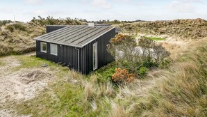 A black cabin with a sloped roof, situated in a grassy area with sparse vegetation. - Lovely home in Hvide Sande with WiFi (Hvide Sande)
