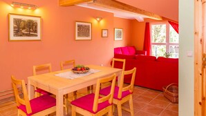 Uma sala de jantar com mesa e cadeiras de madeira, um sofá vermelho e quadros nas paredes.