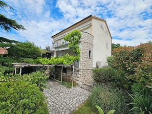 A two-story building with a stone facade, a balcony with vines, and a paved courtyard. - Holiday apartment directly by the sea (Novi Vinodolski)