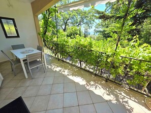 A balcony with a table and chairs, surrounded by greenery and a view of trees. - Holiday apartment directly by the sea (Novi Vinodolski)