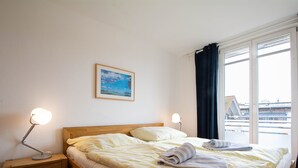 Habitación de hotel con una cama, dos lámparas de noche, una mesita de noche, un cuadro enmarcado en la pared y una ventana con cortinas.