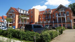 Un edificio residencial de varios pisos con balcones, coches aparcados y un cielo despejado.
