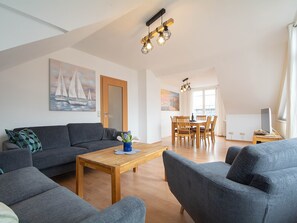 Un vaste espace de vie comprenant un canapé, une table basse et une table à manger avec des chaises. Un tableau orne le mur, ainsi qu’une porte et une fenêtre avec des rideaux.