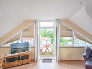 Une pièce comprenant un meuble de rangement en bois pour les appareils multimédias, un canapé en cuir et une grande fenêtre donnant sur un balcon et des immeubles.