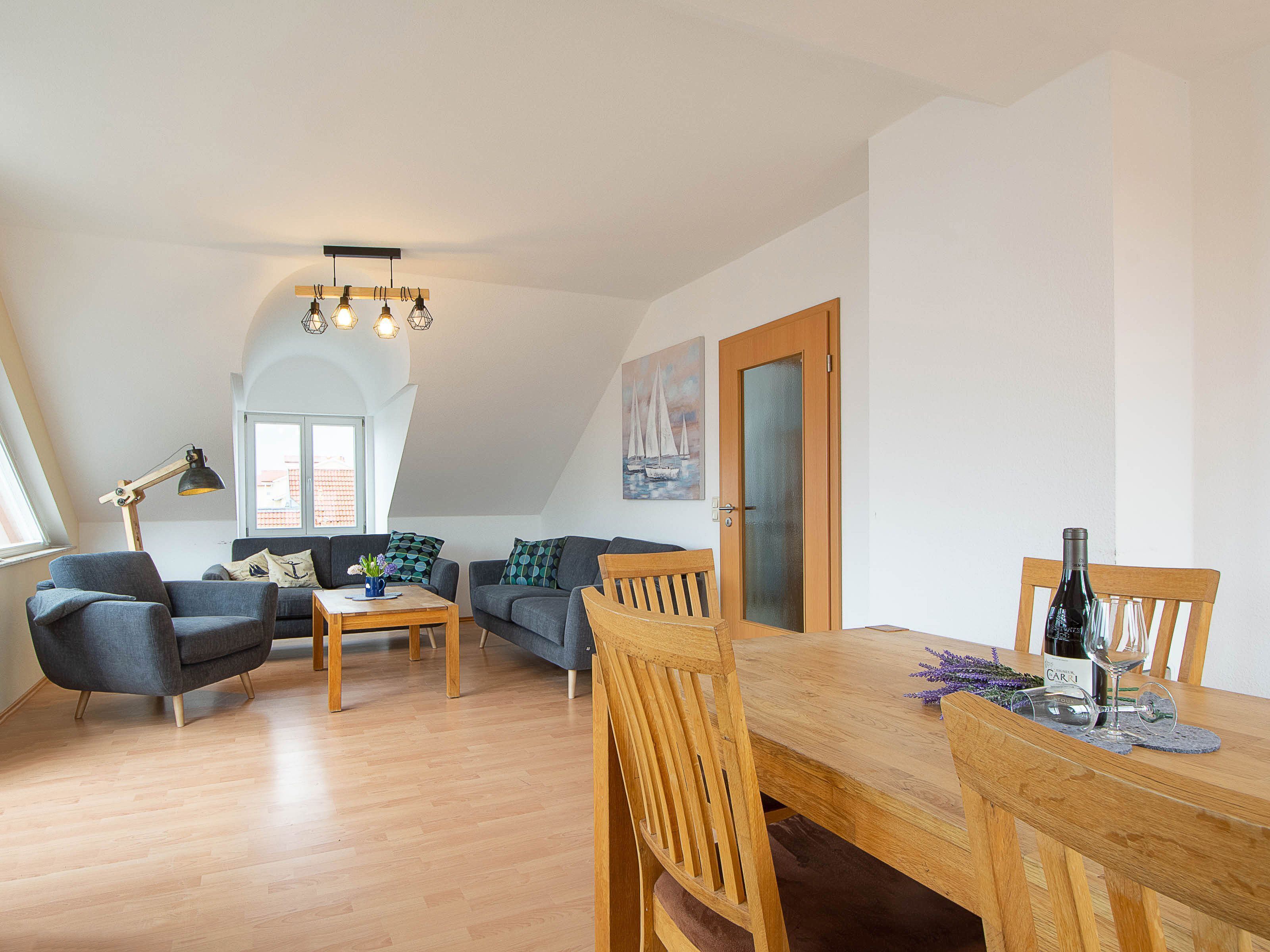 Een ruim loft appartement met een eetgedeelte, twee banken, een houten eettafel en een groot raam.