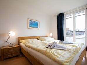 Una habitació d'hotel amb llit, dues làmpades de nit, una tauleta de nit, un quadre al mur i una finestra amb cortines.