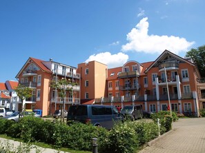 Un edifici residencial de diverses plantes amb balcons, cotxes aparcats i un cel serè.