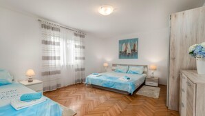 A bedroom with a wooden herringbone floor, a bed with blue bedding, two bedside tables with lamps, a painting of sailboats, and a wooden wardrobe. - Cozy apartment in Dobrinj with WiFi (Dobrinj)