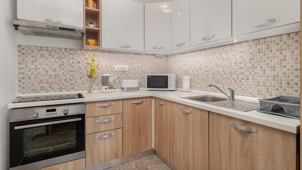 A modern kitchen with white cabinets, a built-in oven, a microwave, and a sink. - Cozy apartment in Dobrinj with WiFi (Dobrinj)