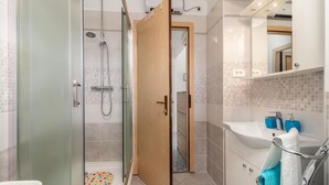 A modern bathroom with a glass-enclosed shower, a wooden door, a white sink with blue soap dispensers, and a mirror above the sink. - Cozy apartment in Dobrinj with WiFi (Dobrinj)
