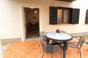 Relax in this serene outdoor space with a round table and four chairs, surrounded by a low wall and a doorway to a cozy interior area.
