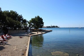 Relax on the pebble beach with sun loungers and umbrellas, surrounded by a tranquil waterfront setting.