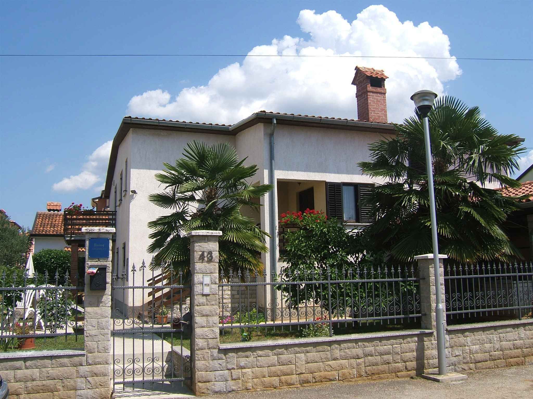 A two-story building with a stone facade, a balcony with red flowers, and a metal fence.